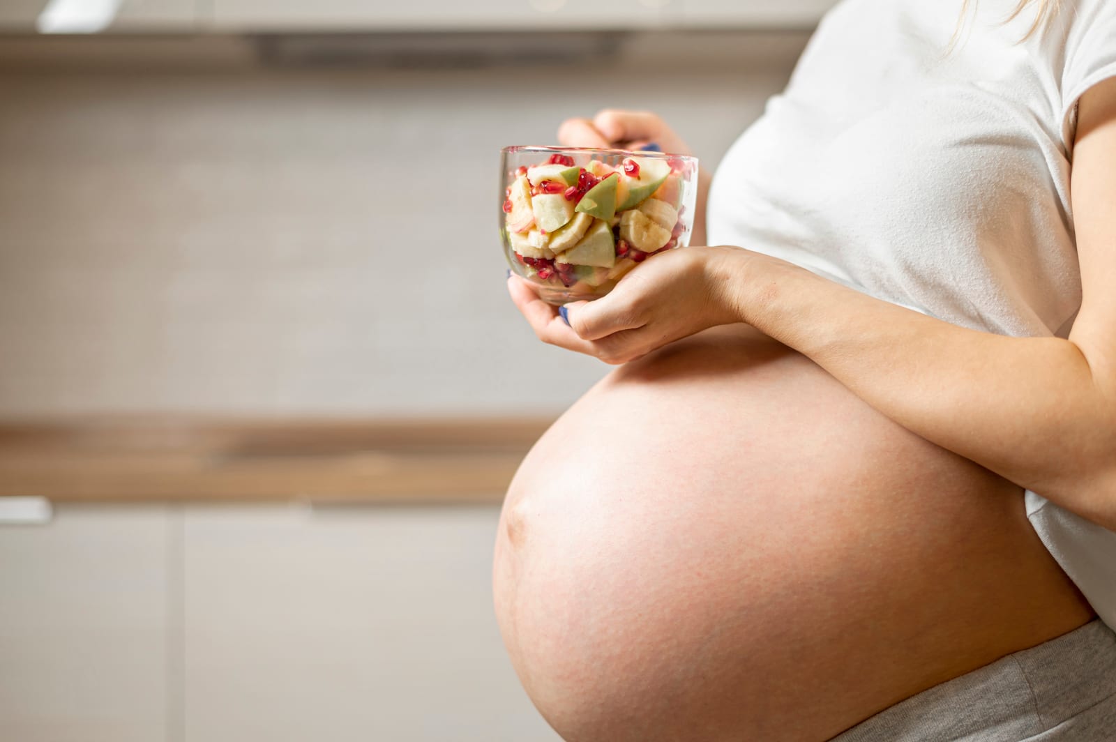 Mujer embarazada sostiene un tazón de fruta fresca en la cocina, alimentación y fertilidad