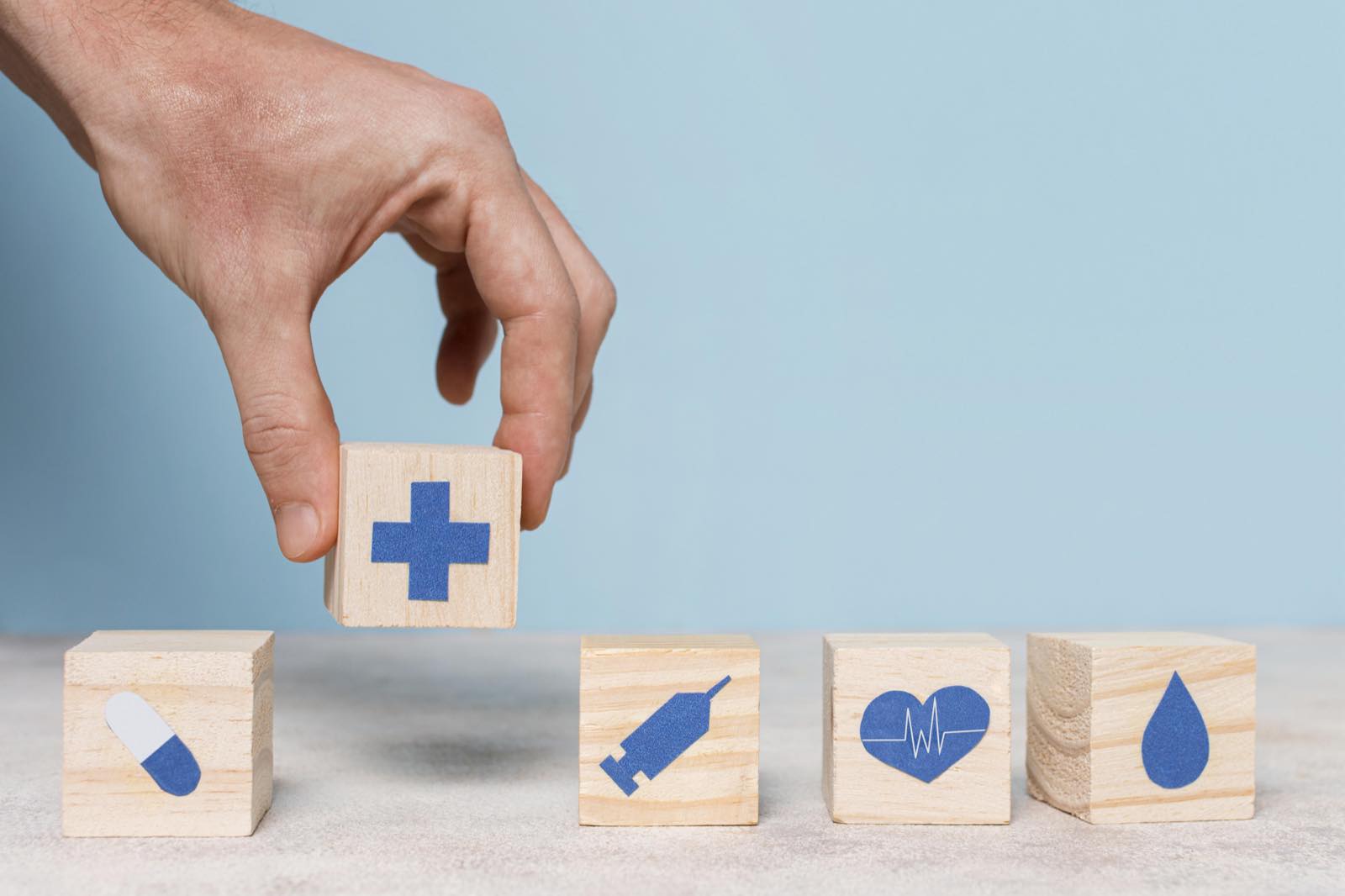 Manos colocando un bloque con una cruz médica junto a otros con íconos de salud