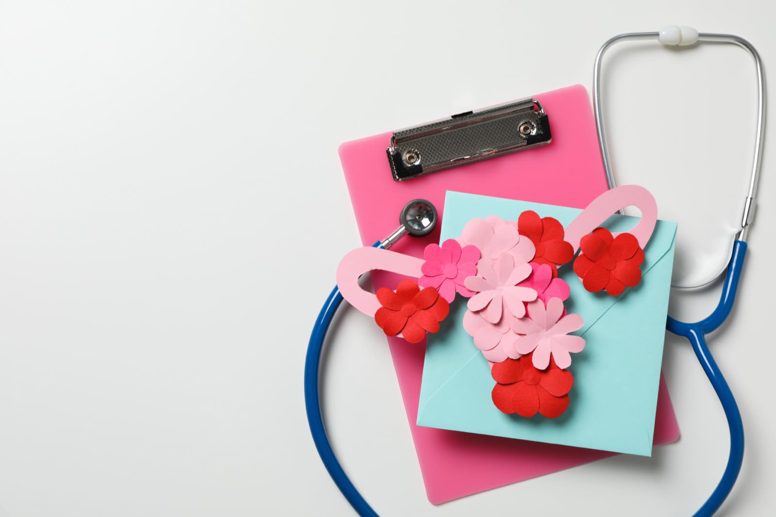 Útero de papel con flores sobre una tabla clínica junto a un estetoscopio