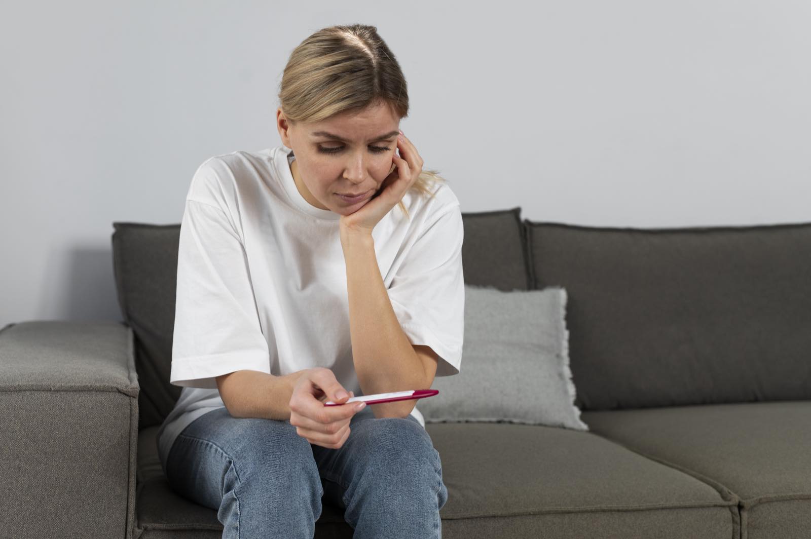 Mujer sentada en un sillón mirando con preocupación una prueba de embarazo