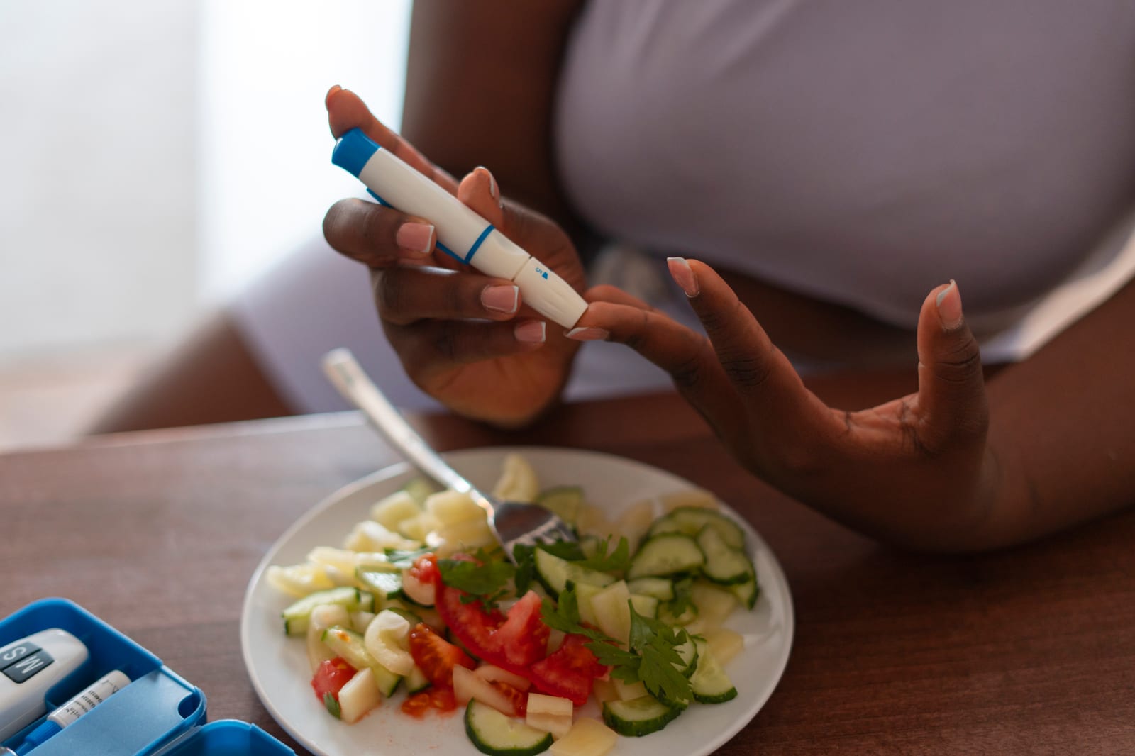 Mujer mide su glucosa con un dispositivo junto a un plato de ensalada, resistencia a la insulina y fertilidad
