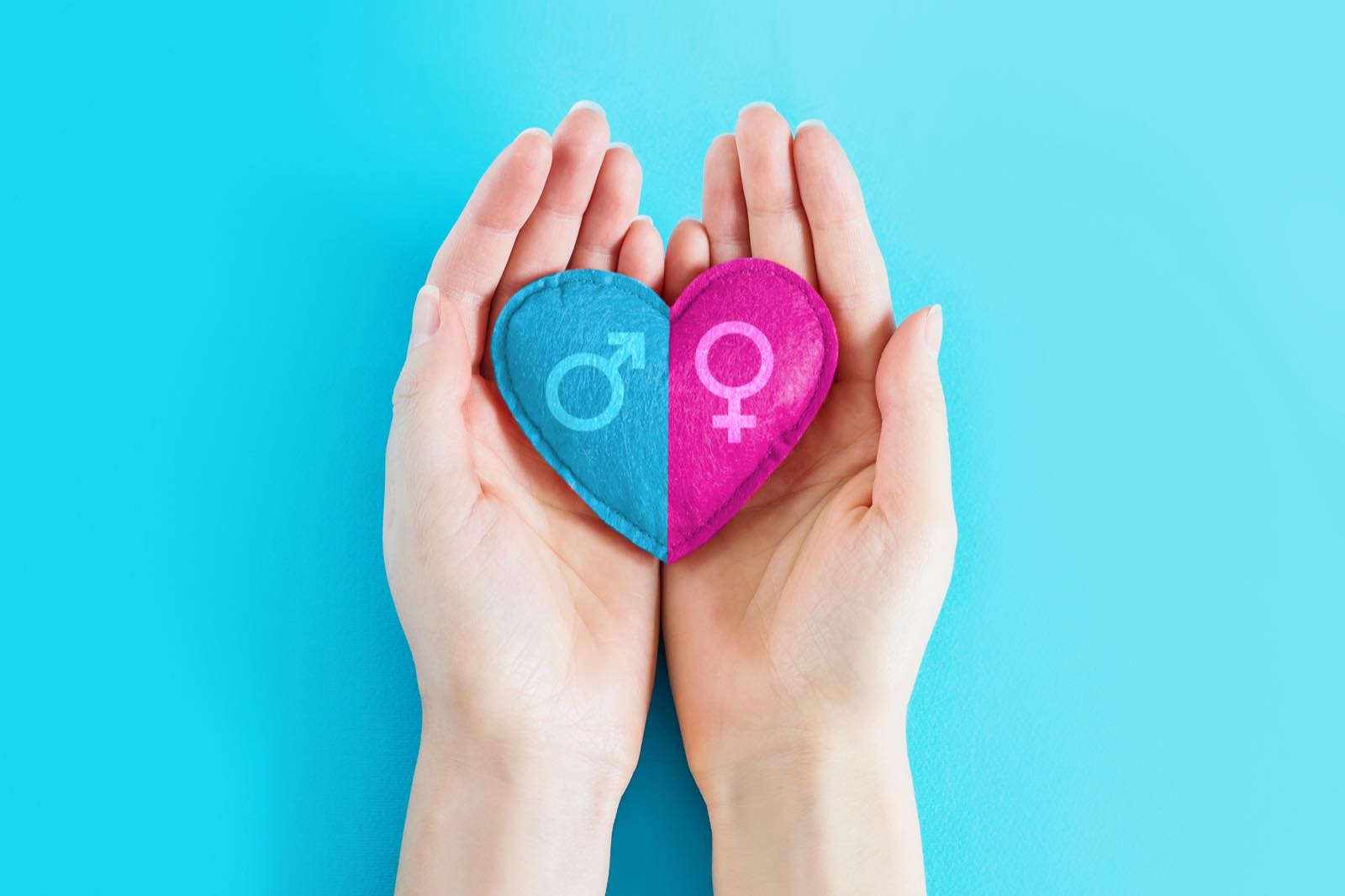 Manos sosteniendo un corazón con los símbolos masculino y femenino